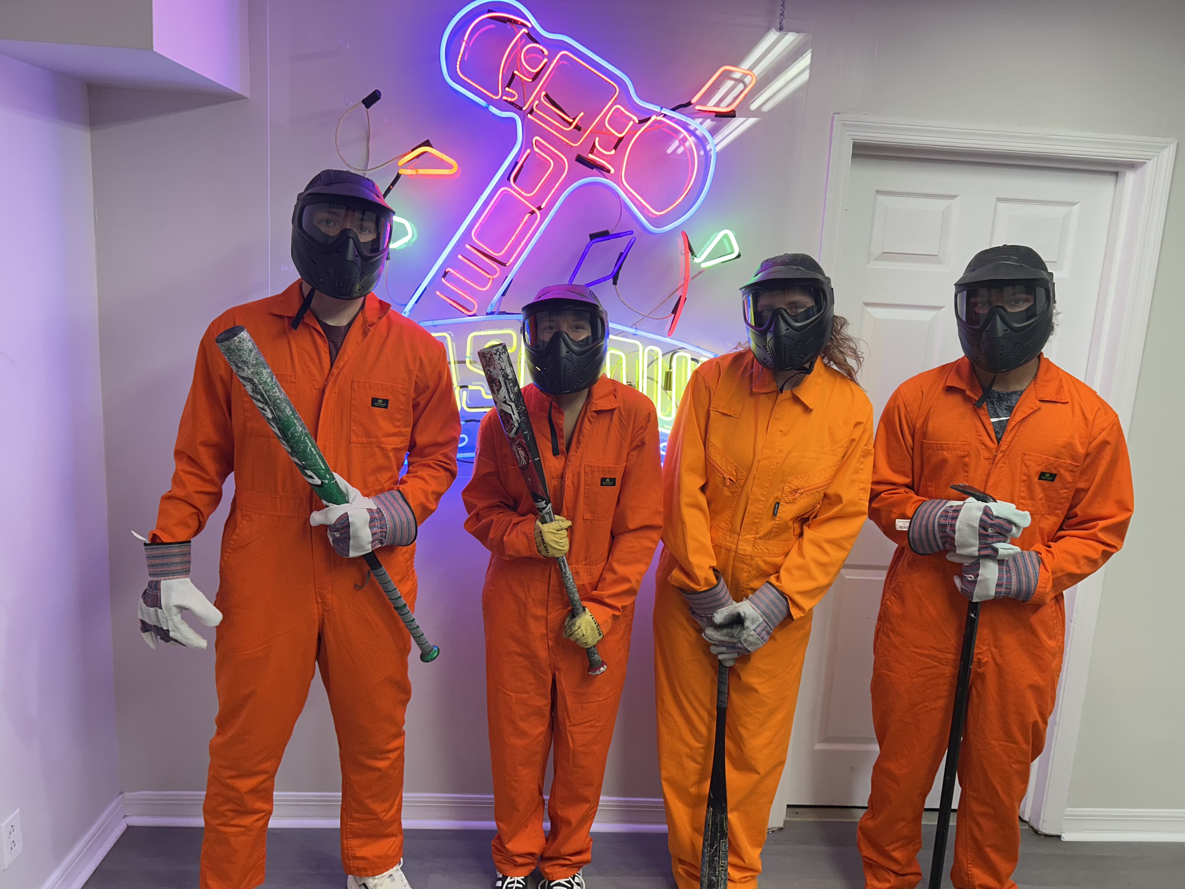 Crash Out Rage Rooms customers in orange jumpsuits selecting baseball bats from a barrel before their smash session