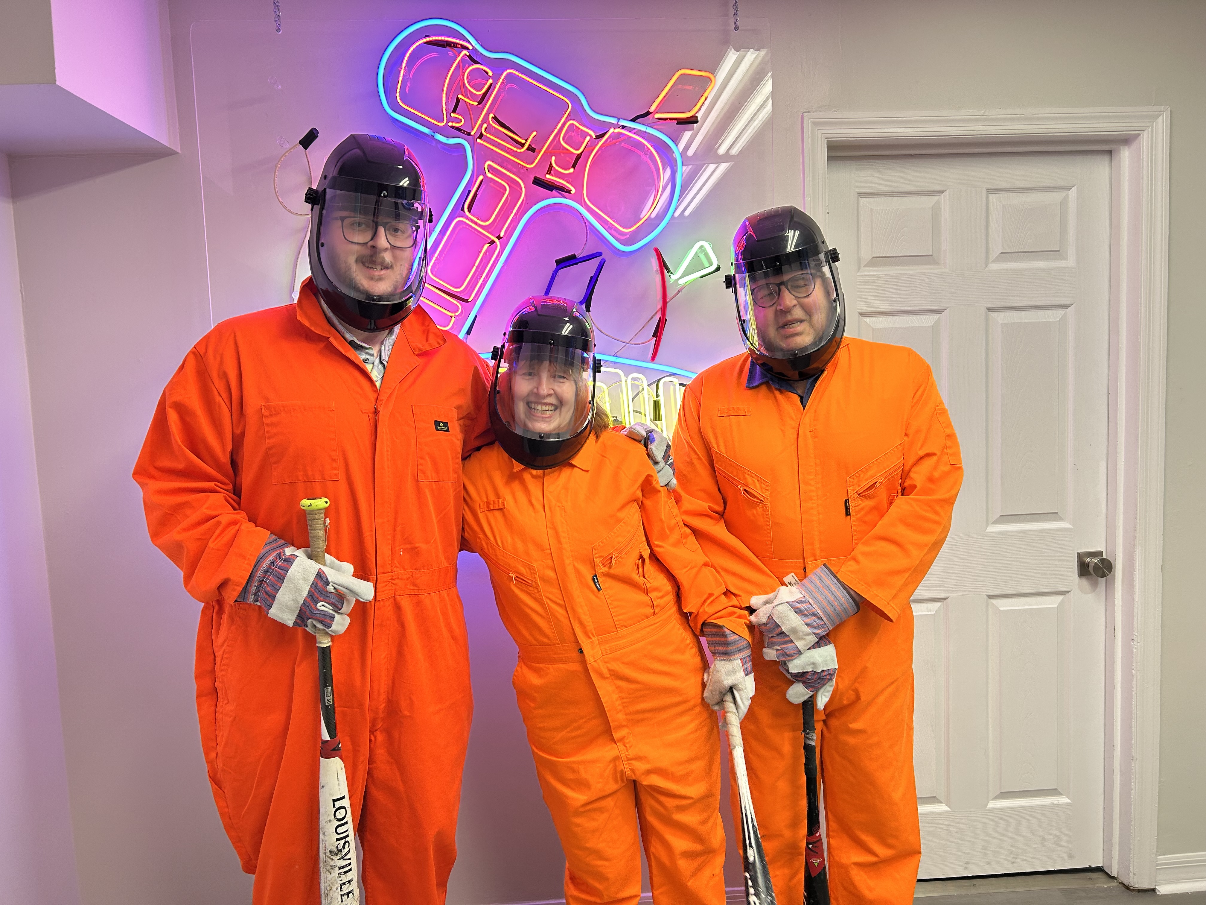 Three smiling Crash Out guests in orange protective jumpsuits ready to enter the smash room