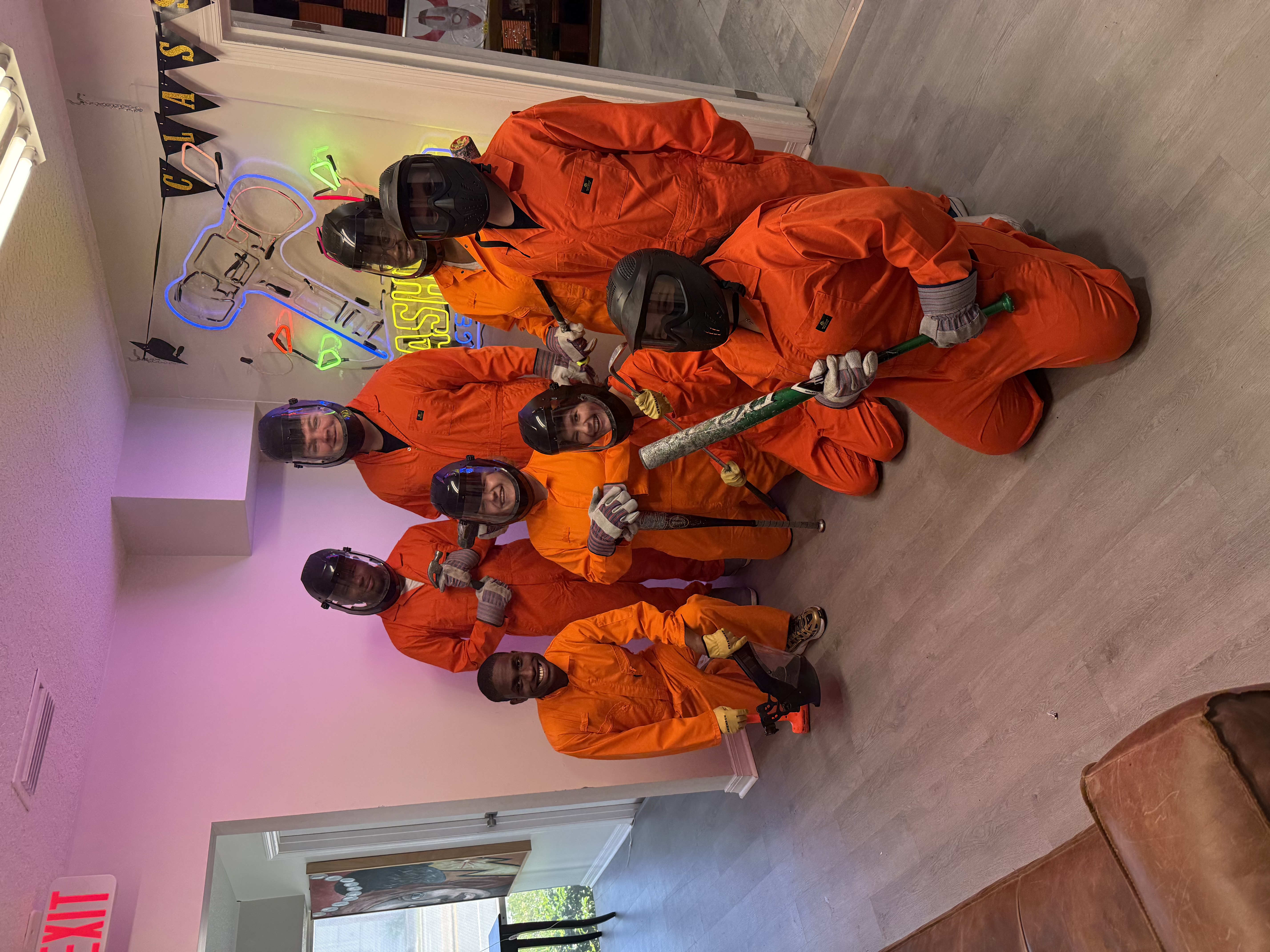 Eight Crash Out customers in full protective orange gear posing together before a smash room session
