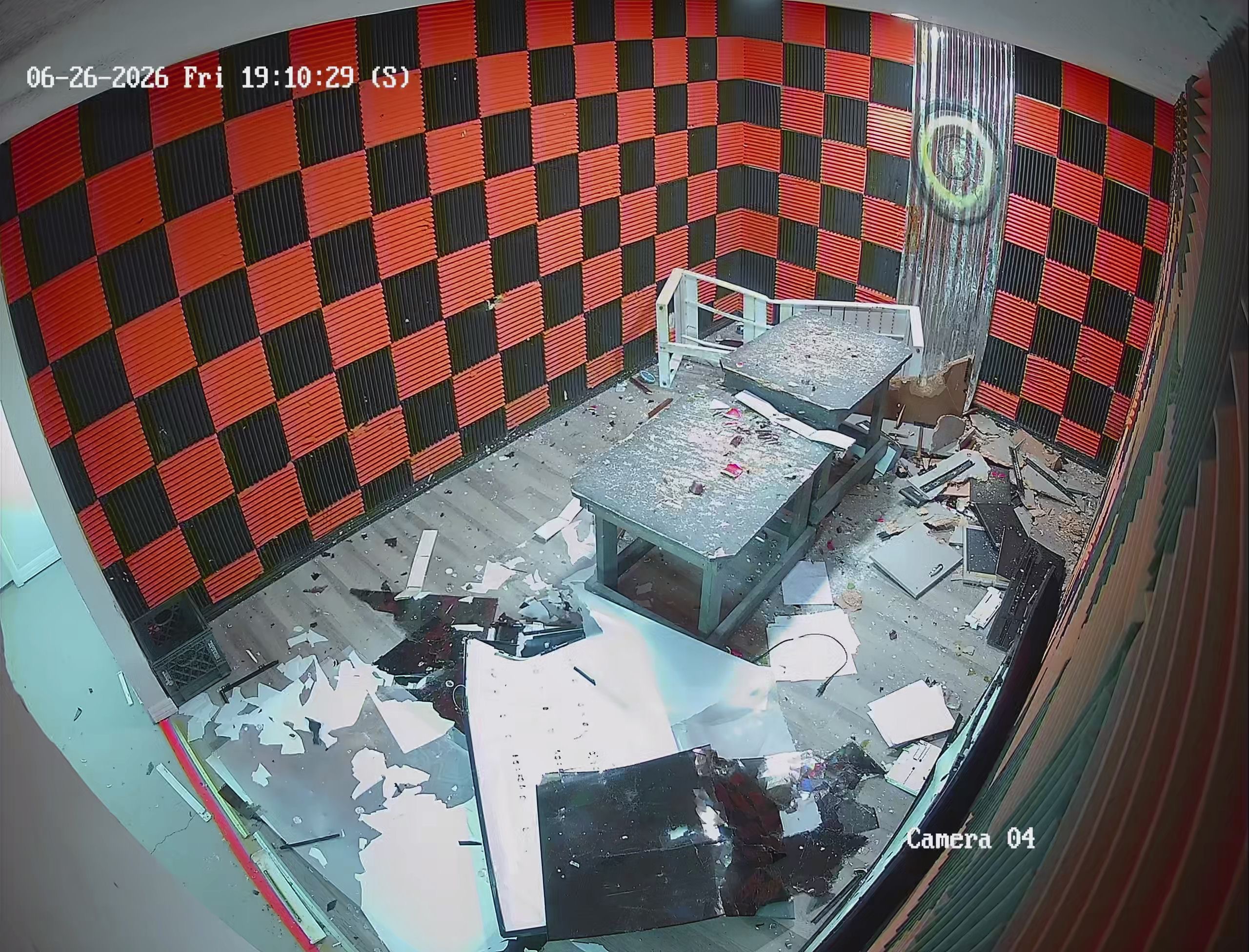 Security camera view of Crash Out rage room after a session — floor completely covered in shattered electronics and debris